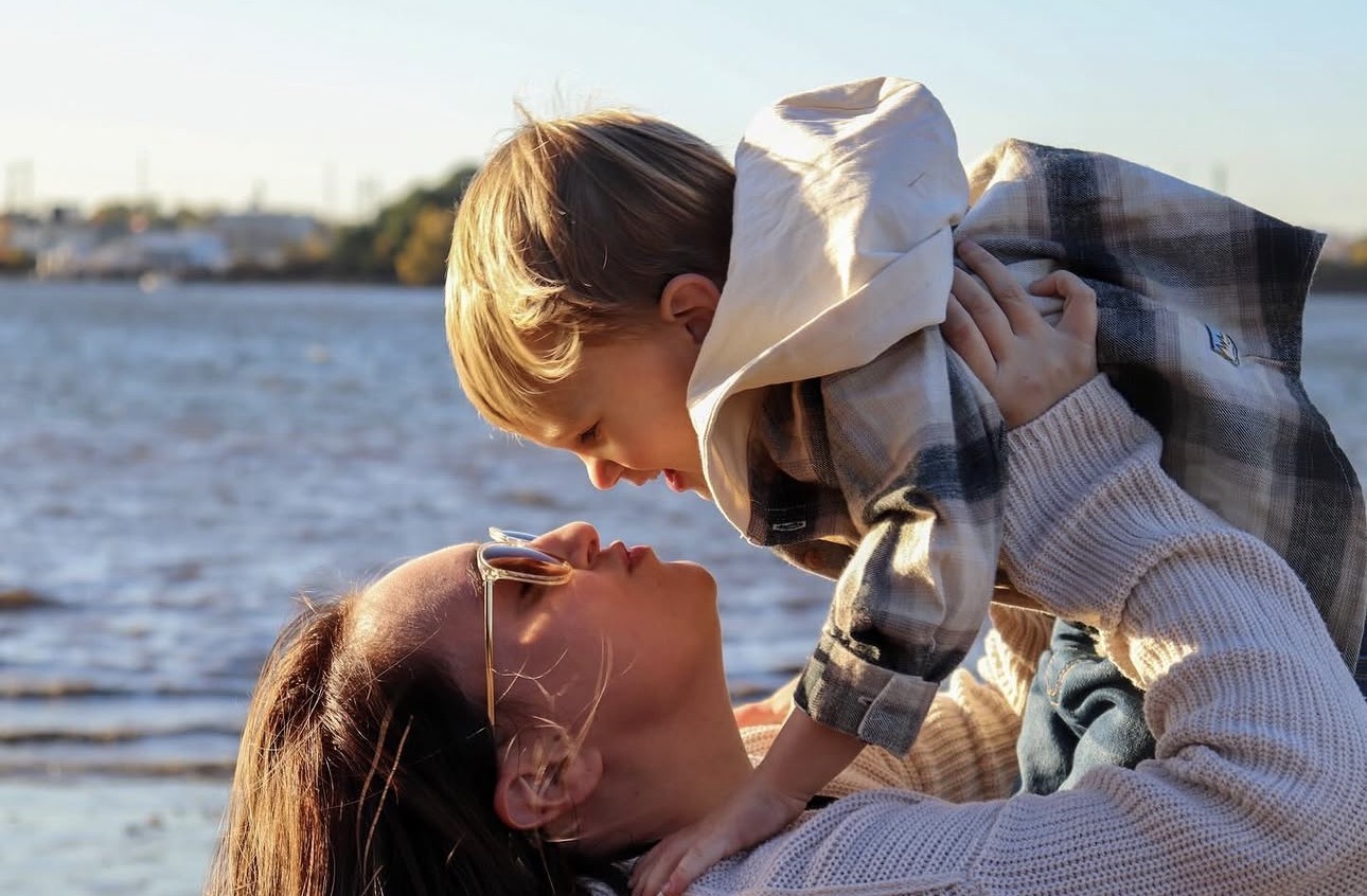Mother lifting her toddler at the waterfront in golden light